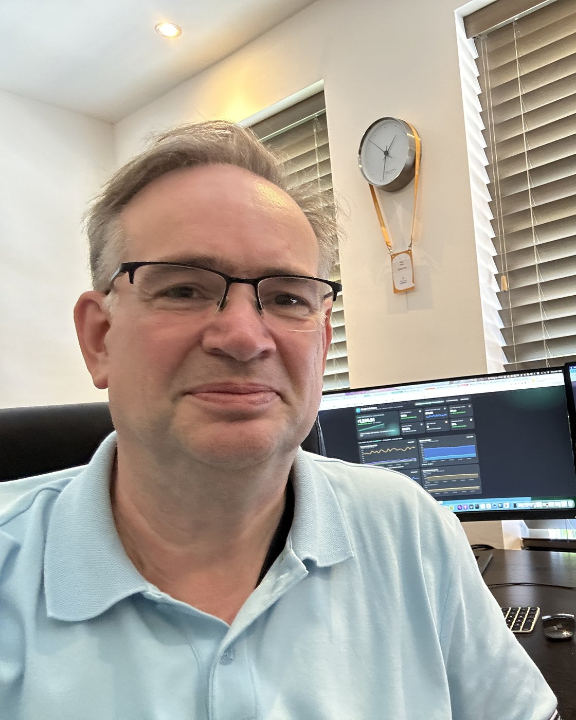 A man in his fifties in glasses and a light-blue polo at his desk, smiling; on the monitors behind him, the subfactory console and this site's landing page; a small silver computer sits on the desk.